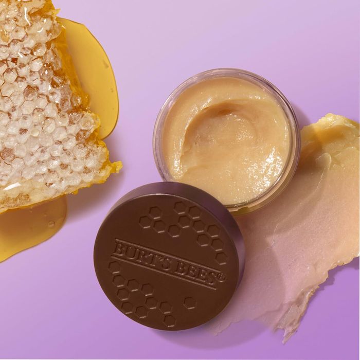 An open jar of Burt's Bees cream, accompanied by a honeycomb and lid, highlighting its natural ingredients in a product display