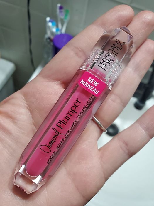Reviewer holding a pink tube of lip-plumping gloss.