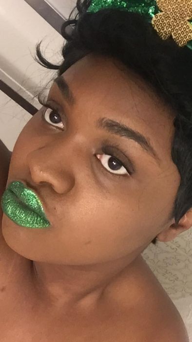 A person striking a selfie pose, flaunting green glittery lipstick and a stylish short haircut.
