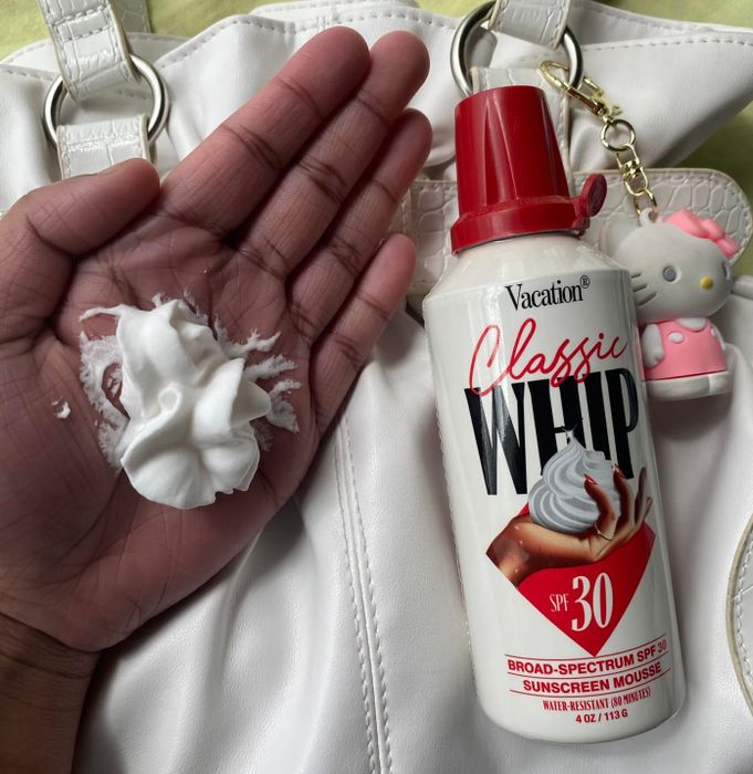 A hand holding a dollop of Vacation Classic Whip sunscreen mousse SPF 30