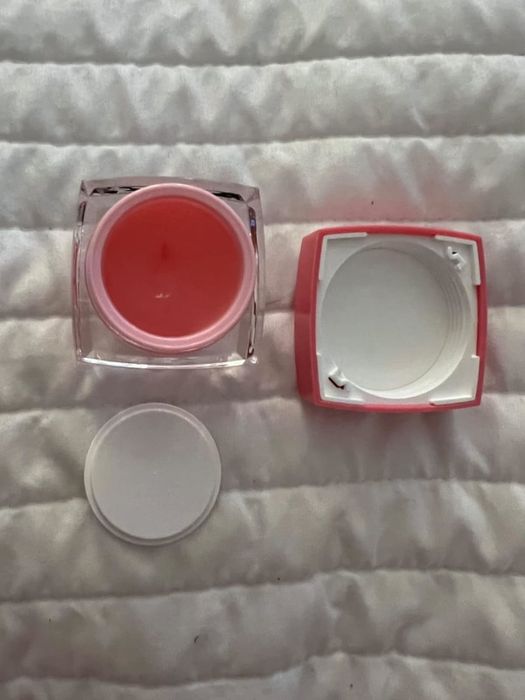 An open jar of skincare product with the lid off, resting on a quilted surface.
