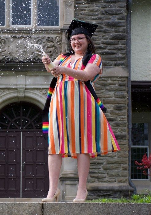 Reviewer joyfully spraying champagne in a rainbow-colored dress for a graduation photoshoot