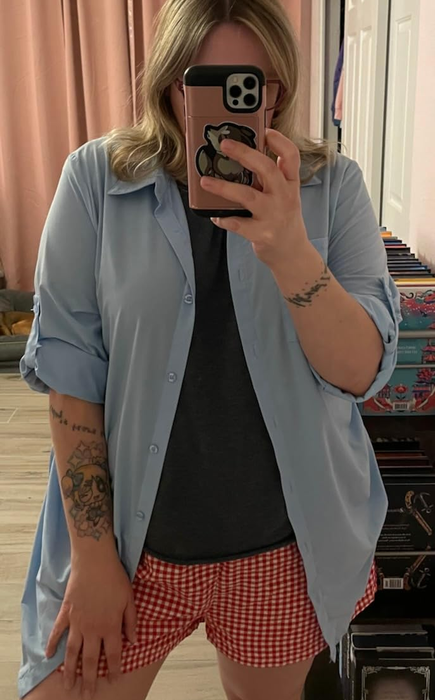 A person dressed in a light blue SPF 50+ button-up shirt layered over a dark t-shirt and red checkered shorts