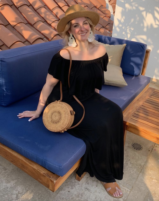 A reviewer models the black dress, accessorized with a straw bag and fedora.