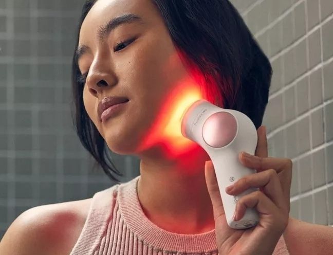 A model using a red light therapy device on their neck and jawline
