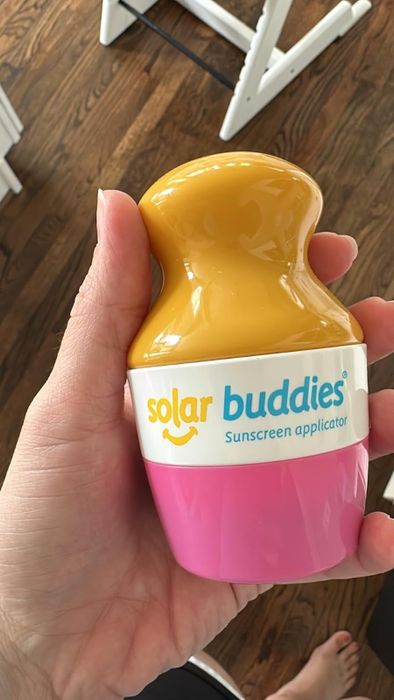 A hand gripping a Solar Buddies sunscreen applicator