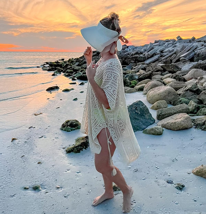 A reviewer on a sandy beach, dressed in a beach cover-up and a sun hat