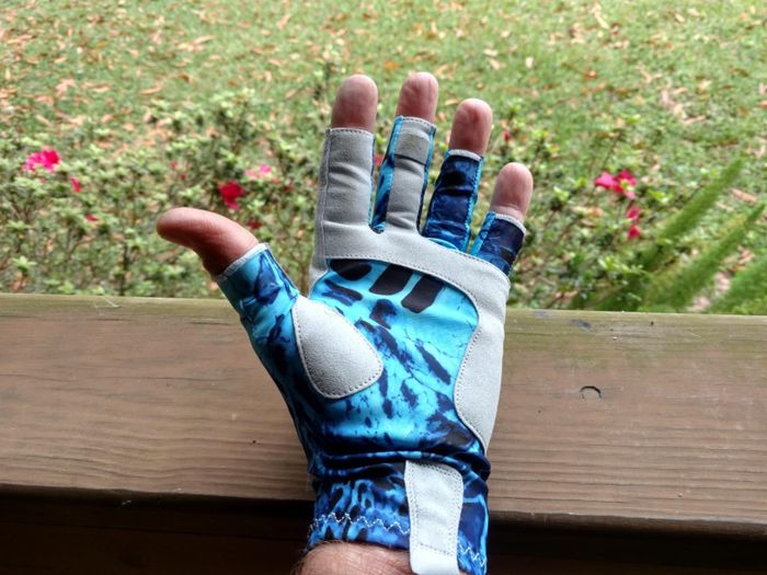 A hand wearing blue and gray fingerless sun protection gloves, shown in an outdoor environment