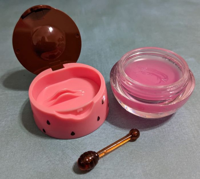 Lip balm containers open with a small applicator stick resting on a table, ideal for shopping articles highlighting beauty products.