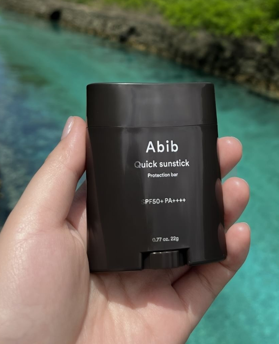 A hand holding the Abib Quick Sunstick SPF50+ with a scenic river in the background