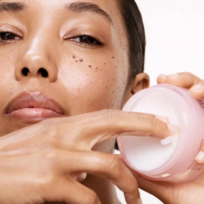Model gently applying skincare cream from a jar to her face