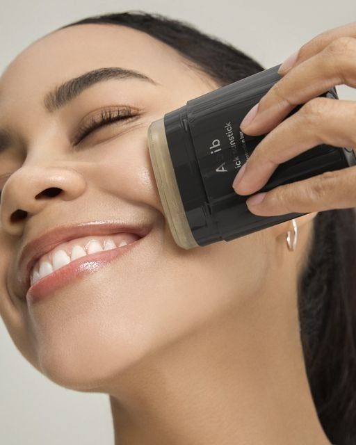 A person applying the sun stick, smiling with their eyes closed