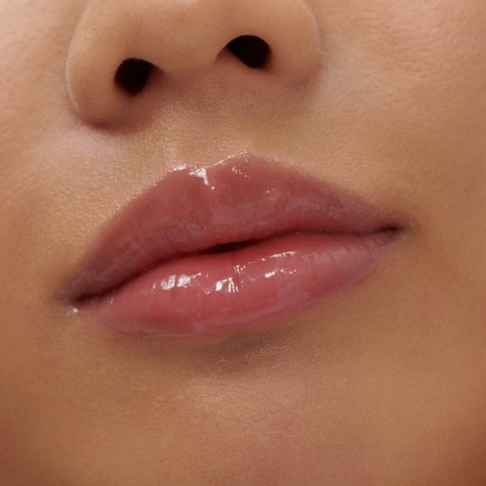 Close-up of glossy, full lips with a slight smile, highlighting a flawless makeup finish.