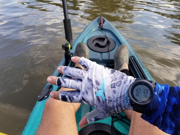 A person in a kayak demonstrates their hand wearing a sun protection glove