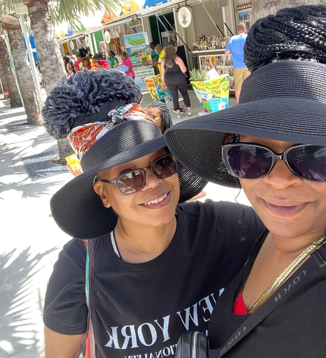 Two individuals smiling while wearing oversized sun hats and sunglasses