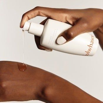 A close-up shot of a person dispensing skincare lotion from a white bottle onto their hand.
