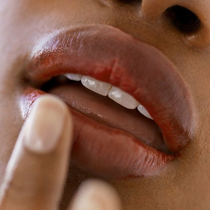 Close-up of a person's lips with slightly smudged red lipstick, a finger gently caressing the lower lip.