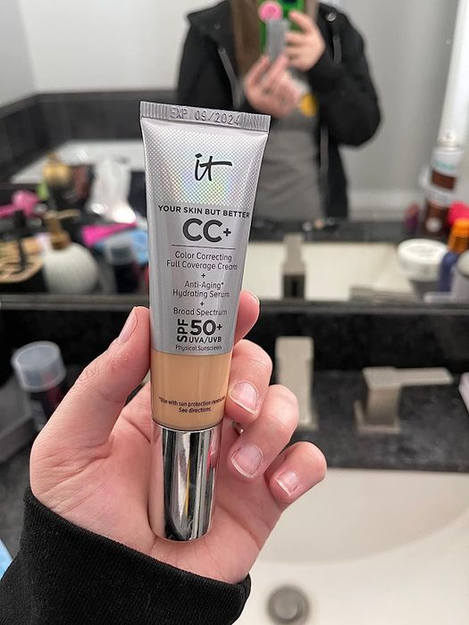 A reviewer holding a tube of IT Cosmetics Your Skin But Better CC+ cream in a bathroom setting