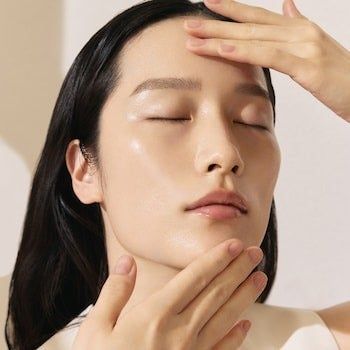 A person, eyes closed, applies skincare to their face in a moment of relaxation. This image is featured in a shopping guide article.