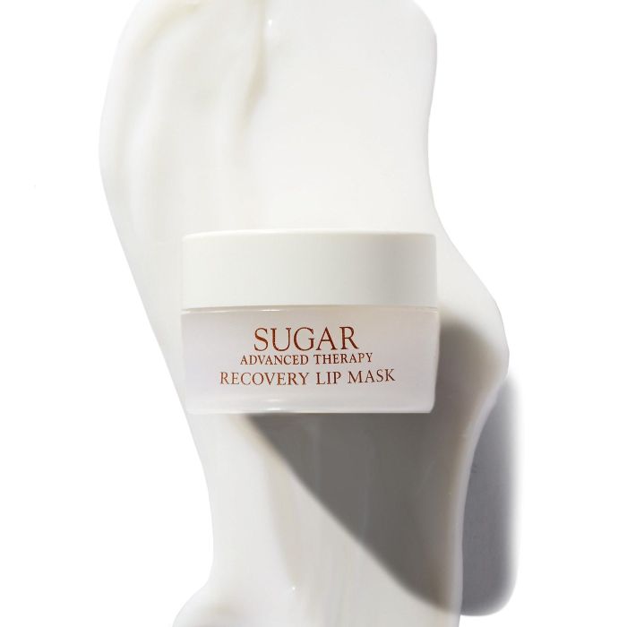 A jar of Sugar Advanced Therapy Recovery Lip Mask surrounded by a creamy texture, showcased in a shopping article.