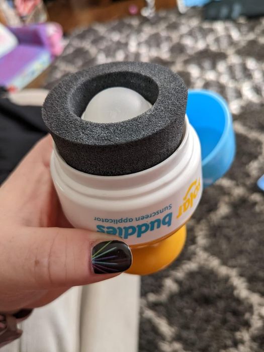 A hand holding a Solar Buddies sunscreen applicator with a black foam top