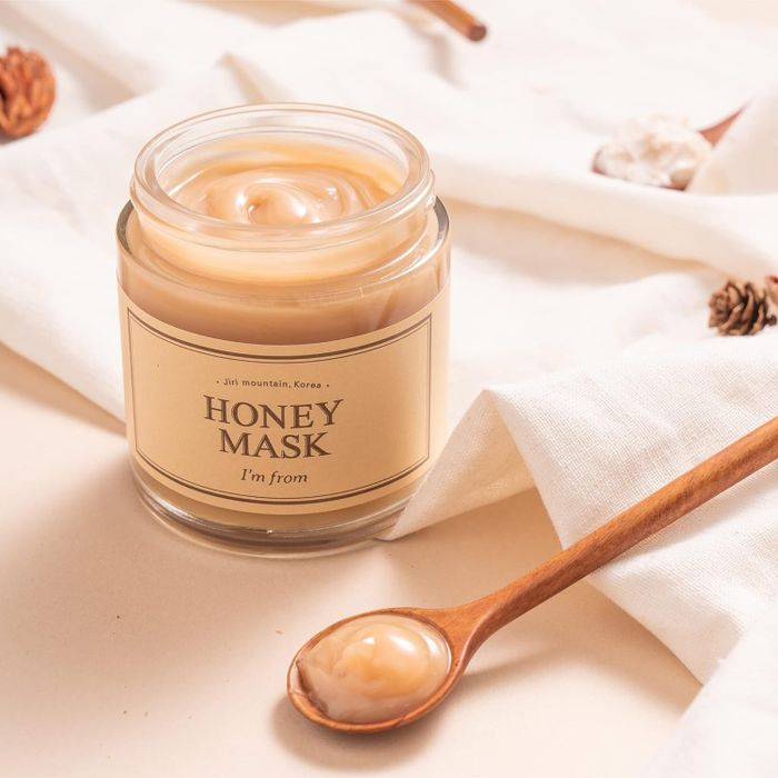 A jar of I'm from Honey Mask with a wooden spoon of the product placed beside it, resting on a fabric surface