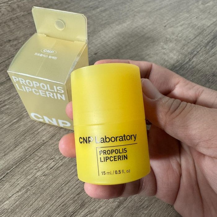 A reviewer holding a CNP Laboratory Propolis Lipcerin container, with its packaging box visible in the background