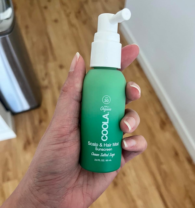A person holding a bottle of Coola Organic Scalp & Hair Mist Sunscreen SPF 30