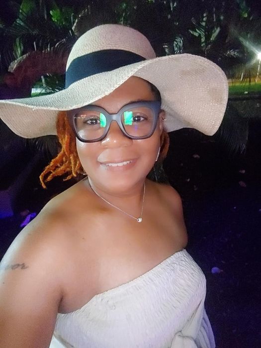 A smiling reviewer posing outdoors in a fashionable wide-brimmed hat