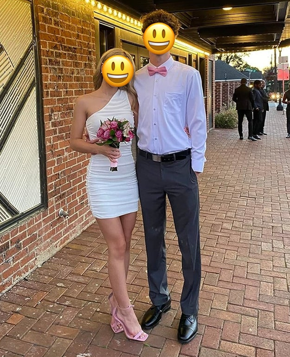 reviewer wearing a white one-shoulder dress posing with her date