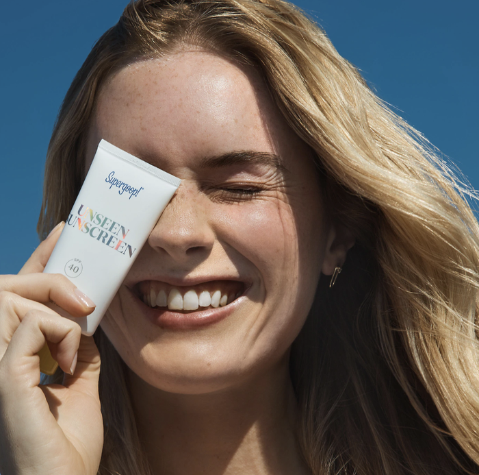 A model showcasing the jar of Supergoop Unseen Sunscreen in hand, ready for a flawless skin day.