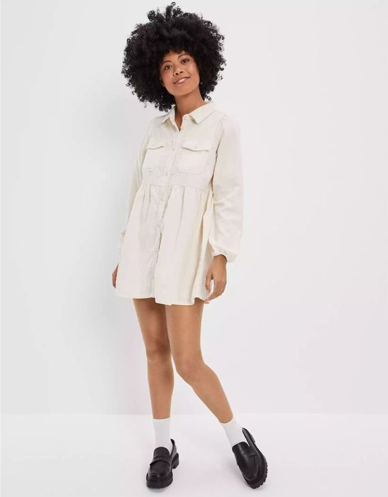 Model wearing a cream-colored corduroy long-sleeve baby doll dress, styled with black oxfords and white ankle socks