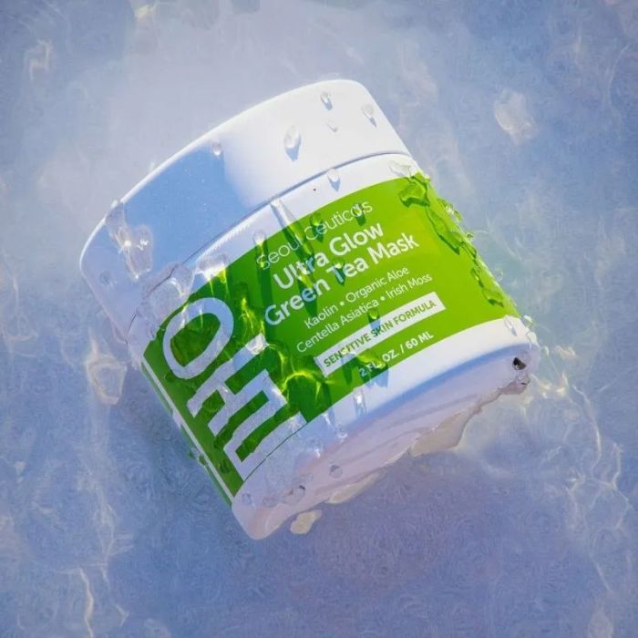 A jar of SeoulCeuticals Ultra Glow Green Tea Mask resting on a reflective surface. The jar features a green label that highlights key ingredients like kaolin, organic aloe, and matcha.