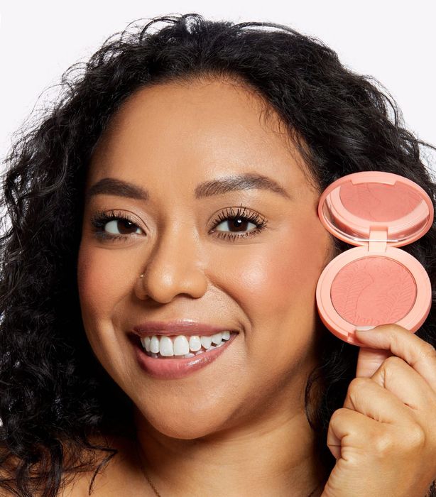 A model holding and wearing Tarte Blush, radiating that natural flush.