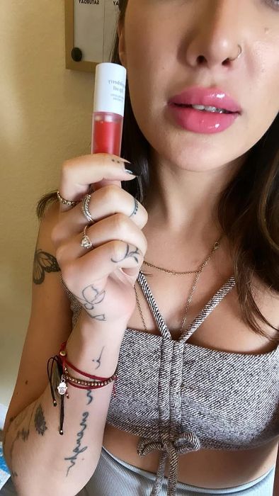 A reviewer holding the appleberry lip oil, with it applied on their lips