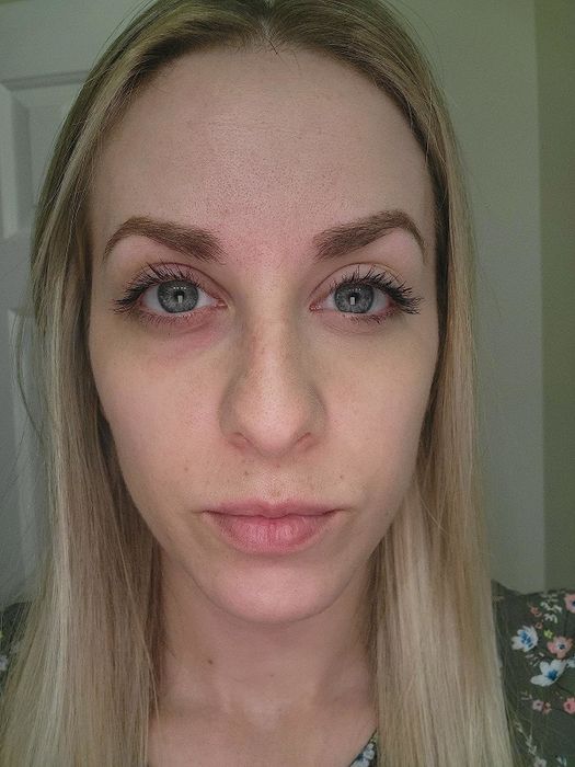 A reviewer demonstrating the difference between one side of their face without foundation and the other side after applying it.
