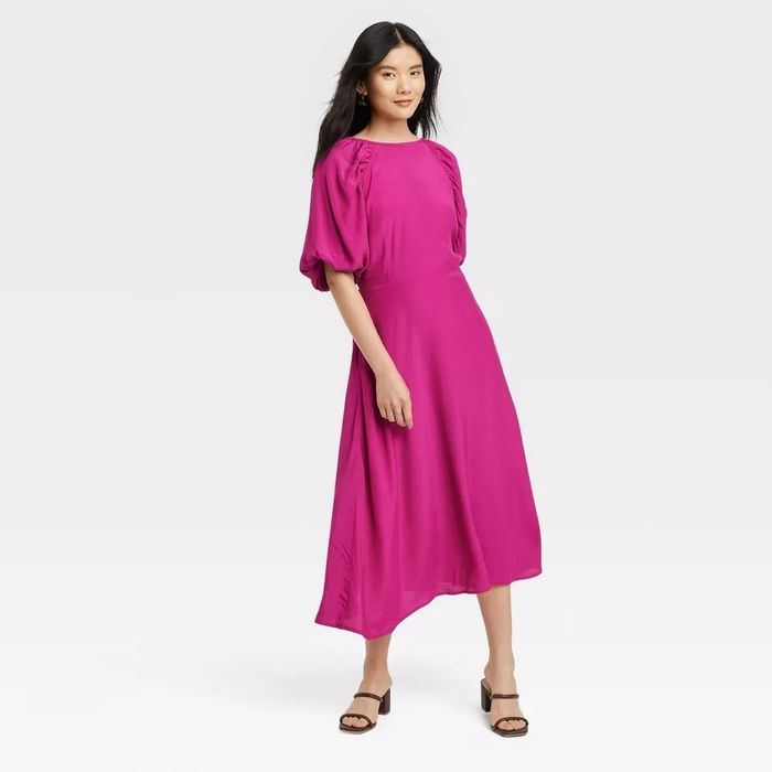 A model rocking a three-quarter puff sleeve pink midi dress paired with black sandals.