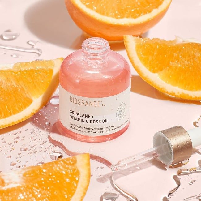 a pink bottle of serum with the cap off and the applicator beside it, surrounded by orange slices