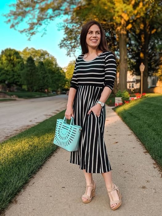 Reviewer in a black striped dress paired with wedges and a blue handbag.