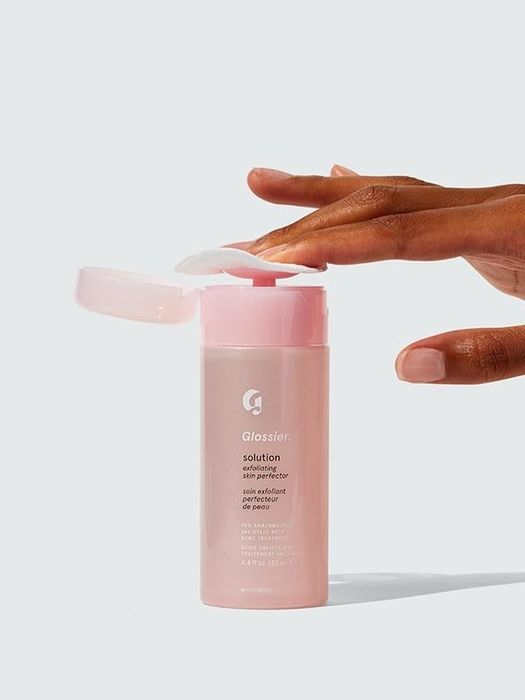Person dispensing the product onto a cotton round from the bottle