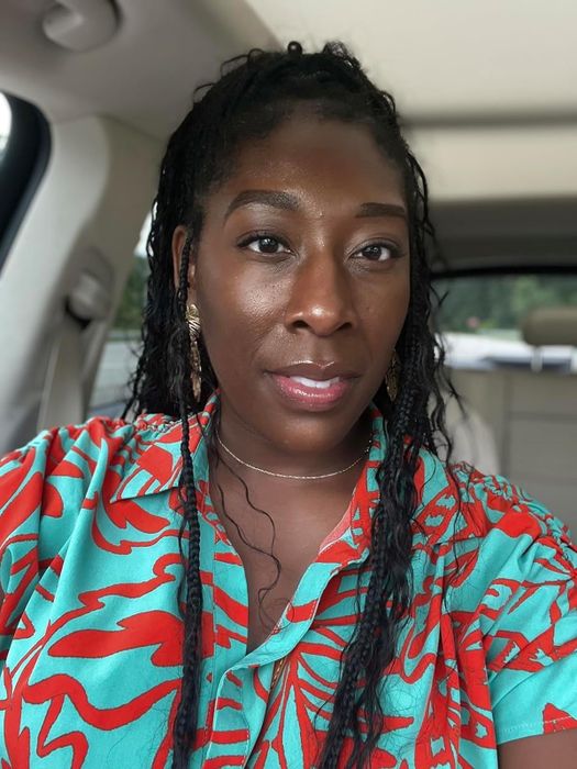 model in a patterned shirt sitting in a car, gazing at the camera while wearing earrings and looking poised
