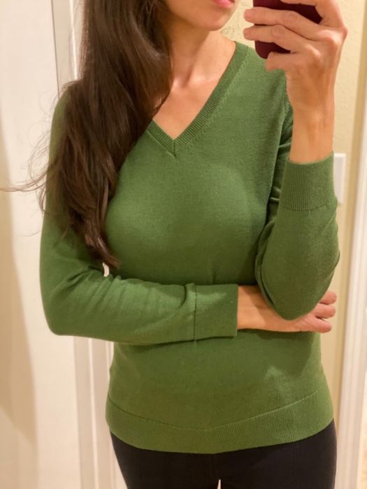 reviewer taking a selfie in a green V-neck sweater, highlighting the outfit’s fit and style