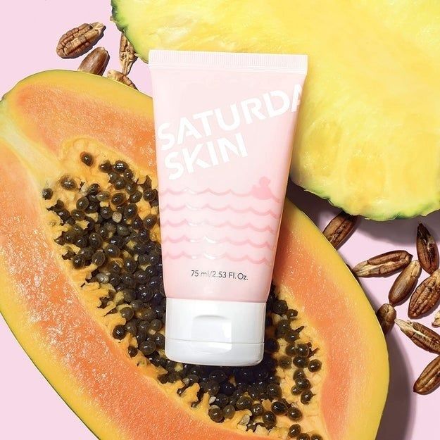 the pink exfoliator bottle with papaya and pineapple in the background