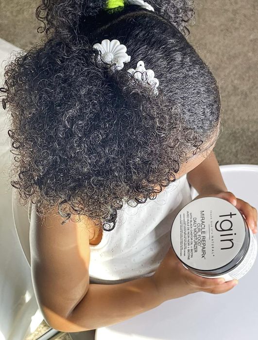 A child model with beautiful, bouncy curls holding the product