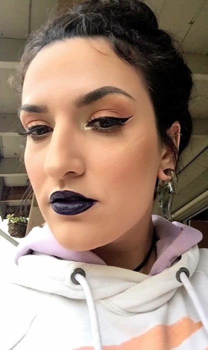 reviewer showcasing a cat-eye look created with the winged eyeliner stamp, paired with dark blue lipstick