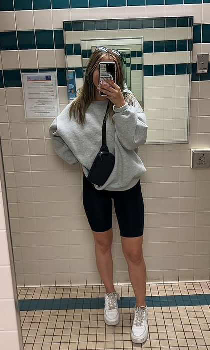 Reviewer snapping a mirror selfie in an oversized sweatshirt paired with cycling shorts, sneakers, and a crossbody bag