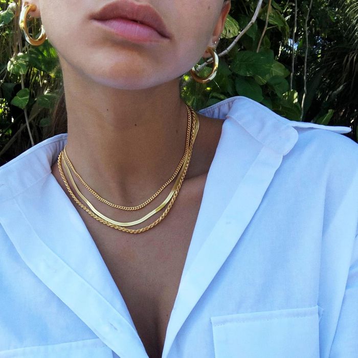 Three gold-toned necklaces with varying chain designs layered on a model's neck