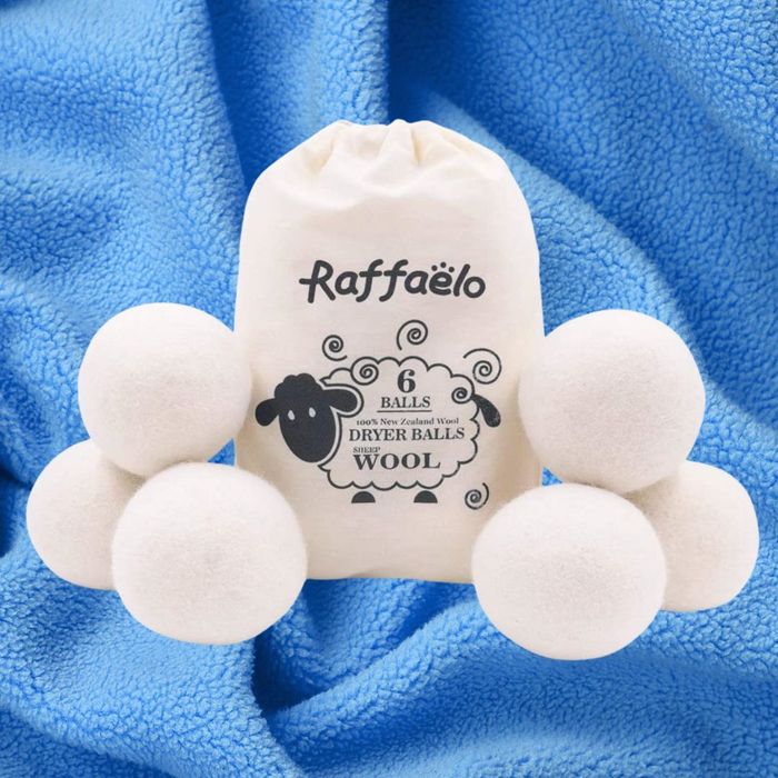 A set of six Raffaelo 100% New Zealand wool dryer balls is shown on a blue fabric. The set is accompanied by a drawstring bag featuring a sheep graphic.