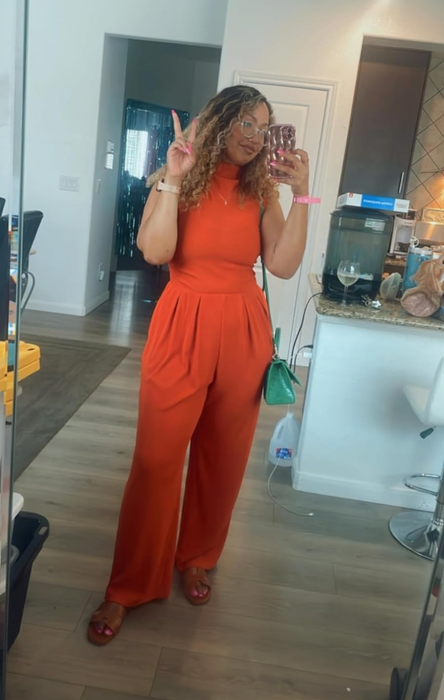 reviewer taking a mirror selfie in an orange jumpsuit with a cinched waist, styled with open-toe sandals