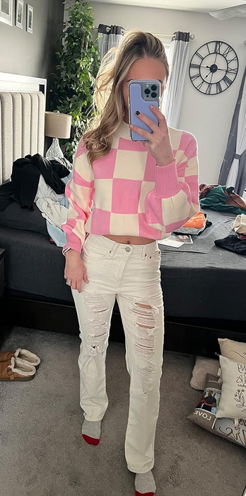 Person in a checkered sweater and ripped jeans capturing a mirror selfie, showcasing a casual outing look